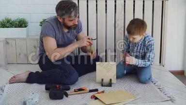 有帮助的儿子正在用手锯锯木片，而他的父亲正在用量筒锯锯木片，并与他交谈